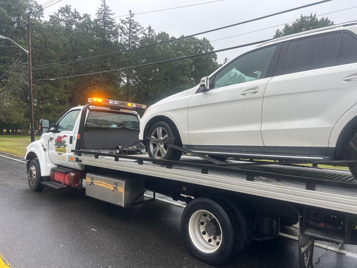 Professional flatbed tow truck transporting a white Mercedes SUV in New Jersey