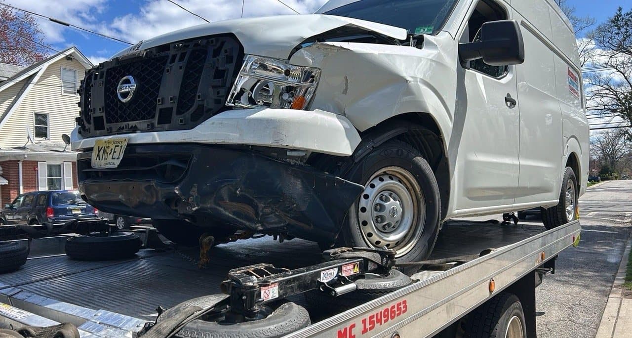 Road Heroes flatbed truck transporting an accident-damaged Nissan commercial van
