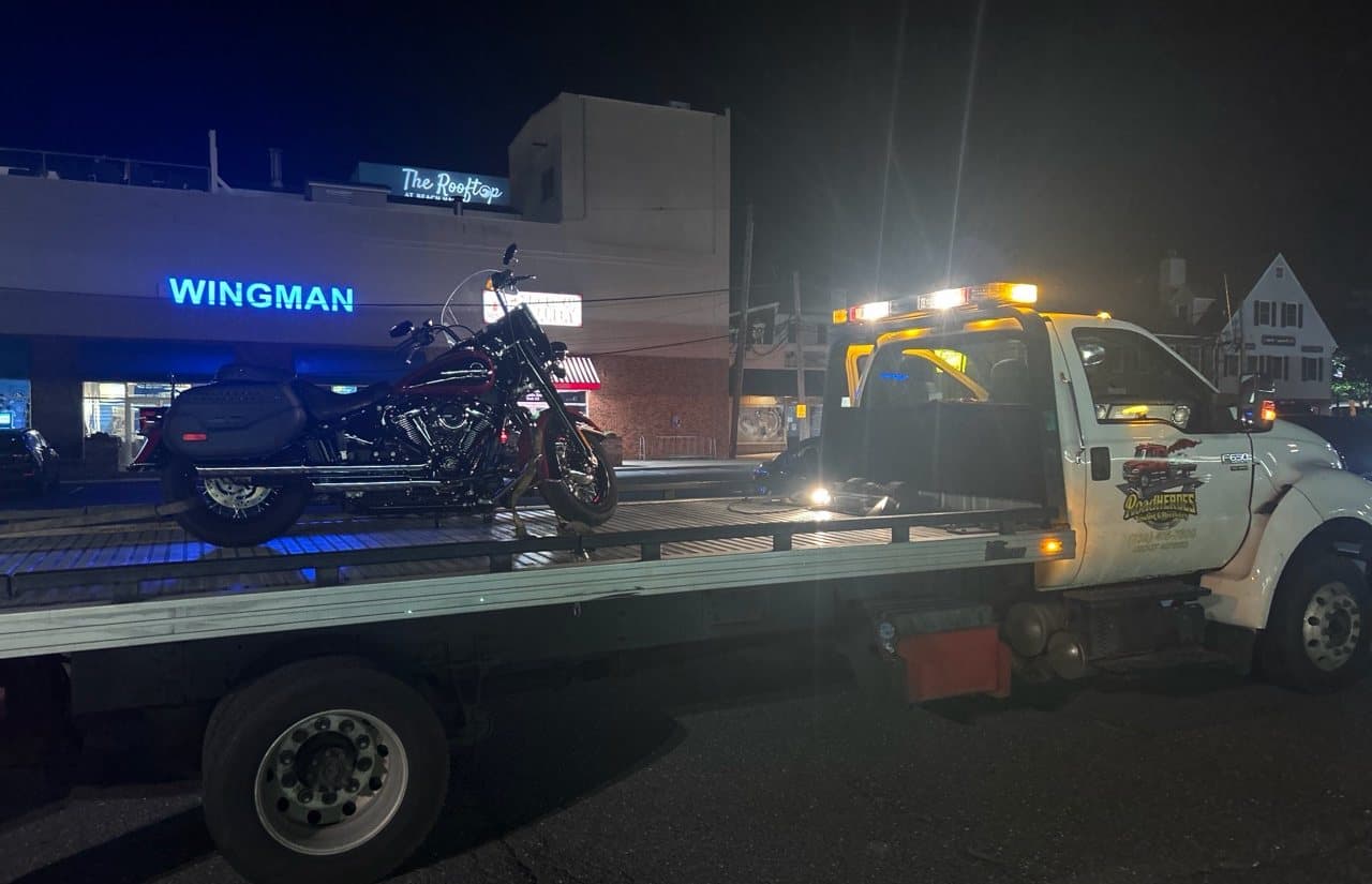 Road Heroes flatbed truck transporting a motorcycle at night